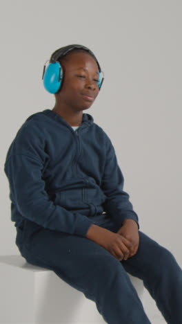 Vertical-Video-Studio-Shot-Of-Boy-On-ASD-Spectrum-Showing-Sensitivity-To-Loud-Noises-Or-Sounds-Putting-On-Ear-Defenders